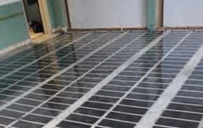 Foto van vloer waarop infraroodverwarming wordt aangelegd. De hele vloer is bedekt met een zwarte spiegelende laag met daarop verticale en horizontale witte lijnen
